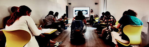 A classroom with several students seated taking notes while a female speaker projects veterinary ultrasound images on a large screen at the back of the room